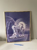 Photo of framed unicorn poster showing a standing unicorn and a foal on a purple starry background with a thin gold frame.
