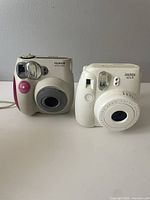 Front view of both cameras side by side on a white surface, showing the Fujifilm Instax Wide 300 (left) and Instax Mini 8S (right).