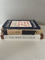 Side view of both cookbooks stacked showing worn dust jacket on 'Mastering the Art of French Cooking Volume Two' and cleaner dust jacket on 'The Way to Cook'.