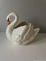 Side view of white ceramic swan planter showing detailed feathers and curved neck with orange and black beak.