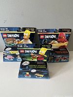Three Lego Dimensions packs including Simpsons Level Pack, Simpsons Fun Pack, and Ninjago Team Pack shown with packaging.