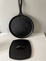 Front view of round cast iron skillet with handle and separate square cast iron press with Lodge branding on the top handle.