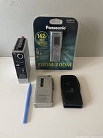 Panasonic digital audio recorder in box, silver Sony and black micro cassette recorders on table with a blue pen for scale