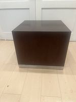 Front view of the square wood block side table with a dark finish and metal strip base on light wood floor.