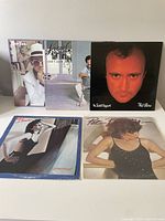 Five vinyl record album covers laid out on a flat surface showing full color images of artists Elton John, Lionel Richie, Phil Collins, and Pat Benatar.