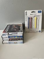 Four Nintendo DS and Nintendo 3DS games stacked vertically with Nintendo DS stylus 5-pack in original blister packaging to the right.
