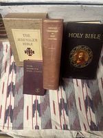 Front view of four hardcover religious books arranged side by side. Books include The Jerusalem Bible in box, New Testament in Greek and Latin, Catholic Commentary on Holy Scripture, and a large Holy Bible with religious image on front cover.