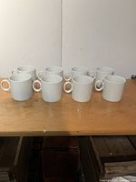 Set of 8 white coffee mugs arranged in two rows on a wooden surface.