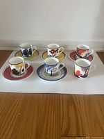 Full set of 6 espresso cups with 5 saucers placed on a flat surface, showing various colorful floral and abstract patterns.