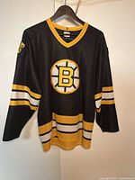 Black vintage Boston Bruins hockey jersey hanging on a wooden hanger against a white background