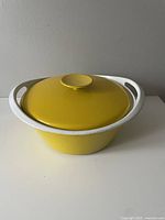 Side view of round enamel cast iron stock pot with yellow lid and white handles, showing overall condition and design.