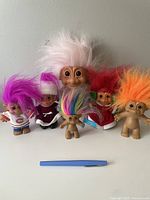 Lot of six Russ troll dolls arranged on a white surface with a pen for scale, showing different colorful hair styles and outfits