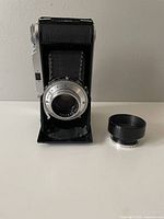 Front view of folding bellows camera extended, lens and separate lens hood visible
