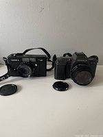 Front view of Yashica 35MF and Yashica 230AF cameras with lens caps removed, showing lenses and camera bodies.