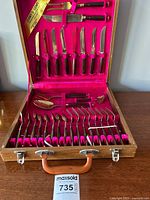 Opened original wood case showing 29-piece set of bronze flatware with rosewood handles arranged in slots inside red fabric lining.