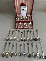 Overall view of 6 Amcora silver plated serving spoons in lined box with 20 souvenir teaspoons in front