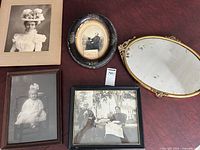 Five antique photographs in different frames on a surface, some frames show wear and damage, including an oval reflective frame with noticeable damage.