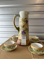 Pitcher with four tea cups and saucers on beige cloth, showing grapevine hand-painted design.