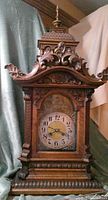 Full front view of the antique wooden mantel clock showing ornate carvings and clock face.