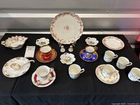 Full view of collection showing all demitasse cups with saucers, decorative plates, salt and pepper shakers, and figurines on black cloth background.