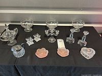 Full lot overview with all items on black cloth, showing creamer, sugar bowl, candlesticks, pink glass dishes, small crystal dishes, heart-shaped box