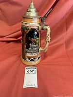 Full view of hand-painted German beer stein with silver-tone lid against red backdrop.