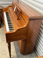 Side angle view showing walnut wood cabinet and brass casters on the piano.