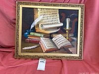 Framed oil painting showing detailed still life with music sheets, quill, books, and candle