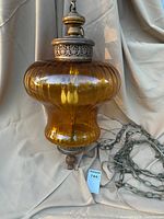 Full view of the amber glass acorn-shaped globe with ornate metal and wooden details and chain.