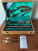 Open wooden box displaying green velvet lining that holds the set of serving cutlery including knives, forks and spoons with rosewood handles.