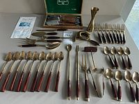 Full view of entire mid-century bronzeware cutlery set with rosewood handles, including spoons, forks, bar tools and knives laid out on table.