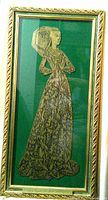 Framed brass rubbing showing a medieval woman figure in detailed gown and headdress on green background.