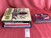 Photo of six stacked books on a pink surface, showing diverse titles about military aircraft and aviation history.