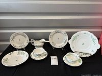 Four plates displayed on stands, one gravy boat, one cup and saucer all decorated in green leaves and blue flowers pattern on white porcelain.