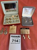 Full view of lot with various pierced earrings arranged on red surface including ones in a red display box, two pairs in separate boxes, and loose pairs on cards.