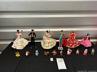 Photo showing full set of six larger national costume dolls and eleven smaller figurines laid on black fabric background.