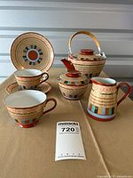 Full view of the porcelain tea set including teapot, creamer, sugar bowl, six cups with saucers, and a salad plate with red base and colorful hand-painted Thousand Faces pattern.