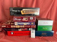 Photo of various boxed board games stacked including Cribbage Set, Bingo, Password, Trivial Pursuit editions, Scattergories, and others