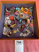 Top-down image of a variety of clip-on earrings in a box showing different colors, shapes, and materials.
