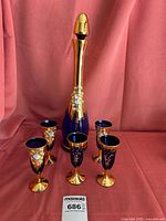 Full set photo showing one tall decanter and five matching aperitif glasses on pink cloth background.