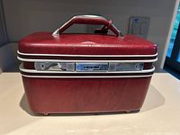 Front view of vintage burgundy Samsonite train case showing hard plastic shell, chrome latches, carrying handle, and Samsonite logo plaque.
