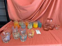 Full set of 19 vintage tumblers displayed on pink fabric background showing variety of sizes, colors, and designs