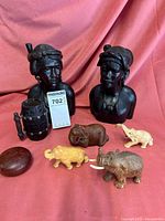 Two wood carved African busts, four small resin elephant figurines in various colors, a small cylindrical wood container with lid, and a round wood piece all displayed on a red cloth background.