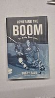 Front cover of the hardcover book titled 'Lowering the Boom: The Bobby Baun Story' showing Bobby Baun skating in Maple Leafs uniform.
