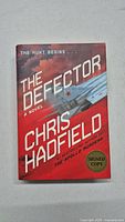 Photo of the book cover titled 'The Defector' by Chris Hadfield with a signed copy sticker.