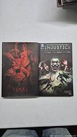 Photo showing both hardcover DC Comics graphic novels: Final Crisis on left and Injustice Gods Among Us on right.