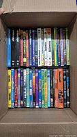 Top-down view of DVDs in box showing a variety of titles and genres including animated and live action films.