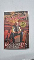 Front cover of the signed first edition book 'Hockey Towns' showing Ron Maclean sitting in an arena.