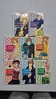 Eight volumes of French manga titled 'L'amour à tout Prix' arranged in three rows on a gray surface showing colorful covers with diverse character illustrations.
