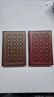 Two hardcover books with decorative leather bindings, diamond pattern and fleur-de-lis on front covers.